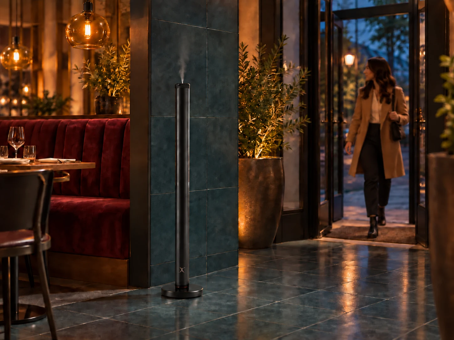 A black X AP40 diffuser at a warmly lit restaurant entrance with teal tile, burgundy seating and an arriving guest