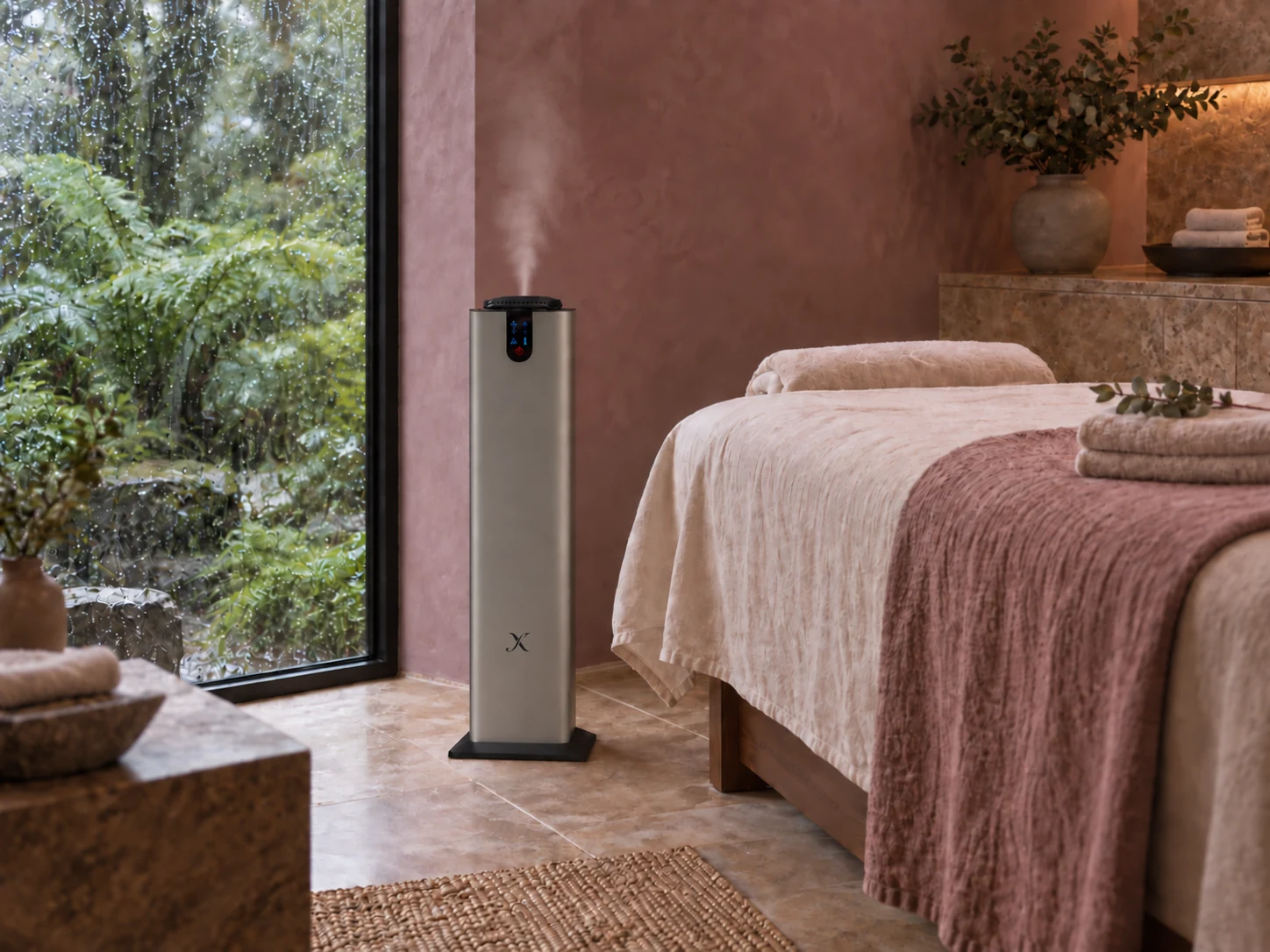 A dark silver X A2000 floor diffuser beside a linen treatment bed in a mauve room overlooking a rain-soaked fern garden