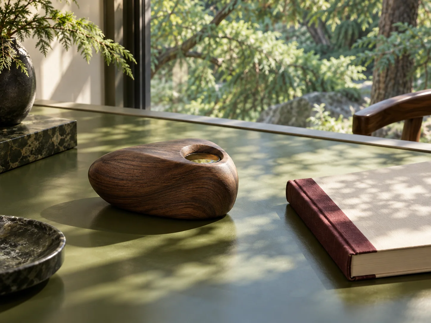 A sculpted walnut fragrance wood diffuser on a green lacquer desk overlooking a cedar garden